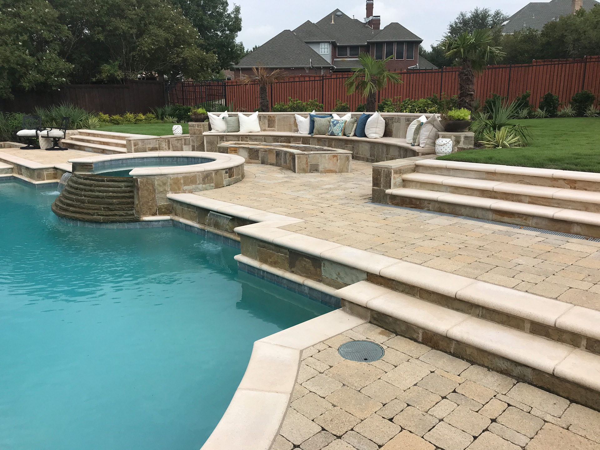 paved patio with a built in fire pit with seating and a pool with hot tub