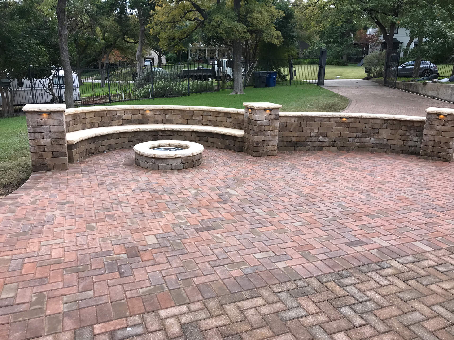 This round fire pit looks gorgeous with a built in bench with wall and a matching paved patio.